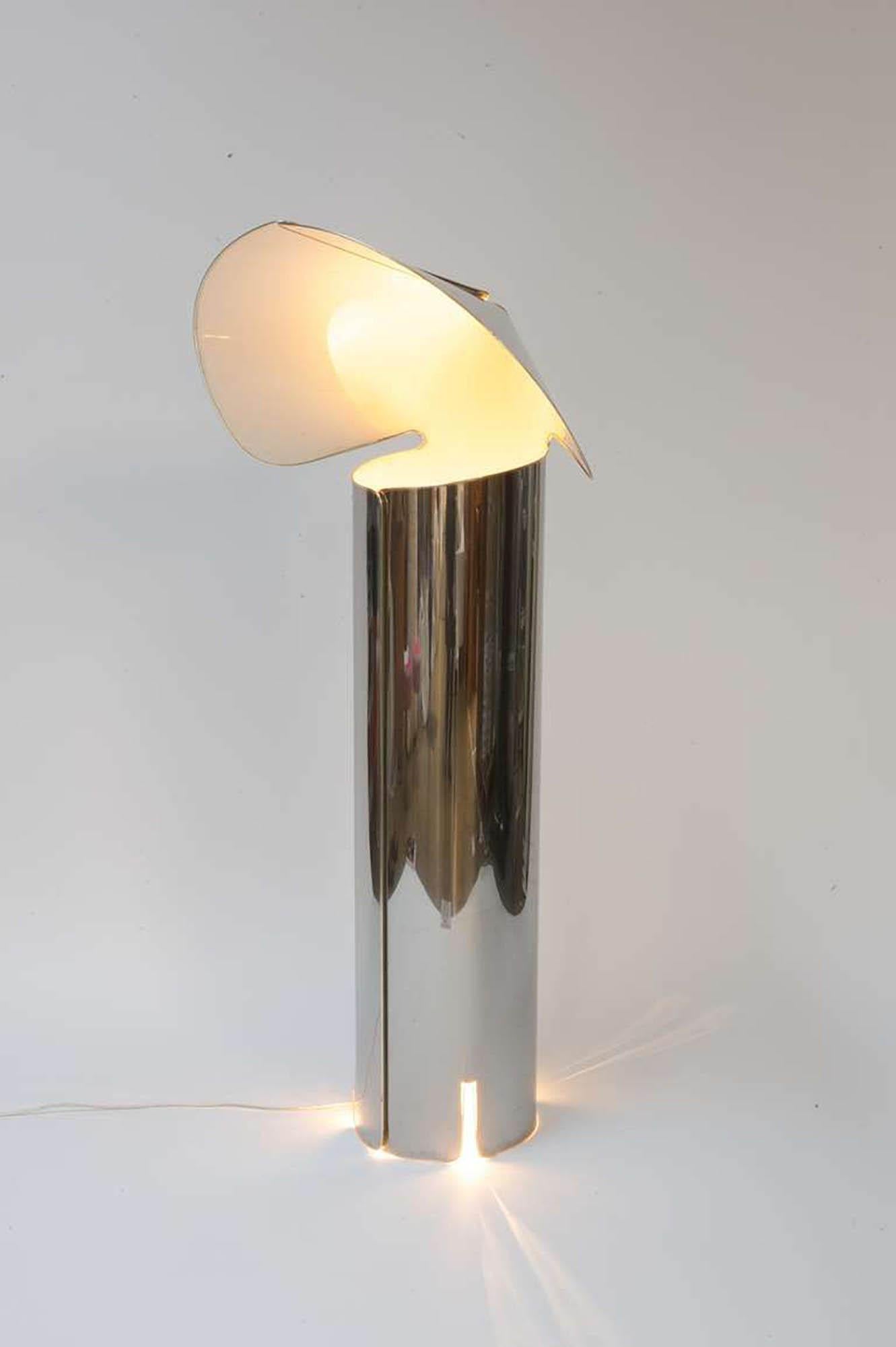 The Chiara floor lamp, designed by Mario Bellini for Flos, originally designed in 1969, is an iconic design consisting of a simple sheet of polished stainless steel that has been cut and rolled into a cylinder. This origami-like structure conceals a