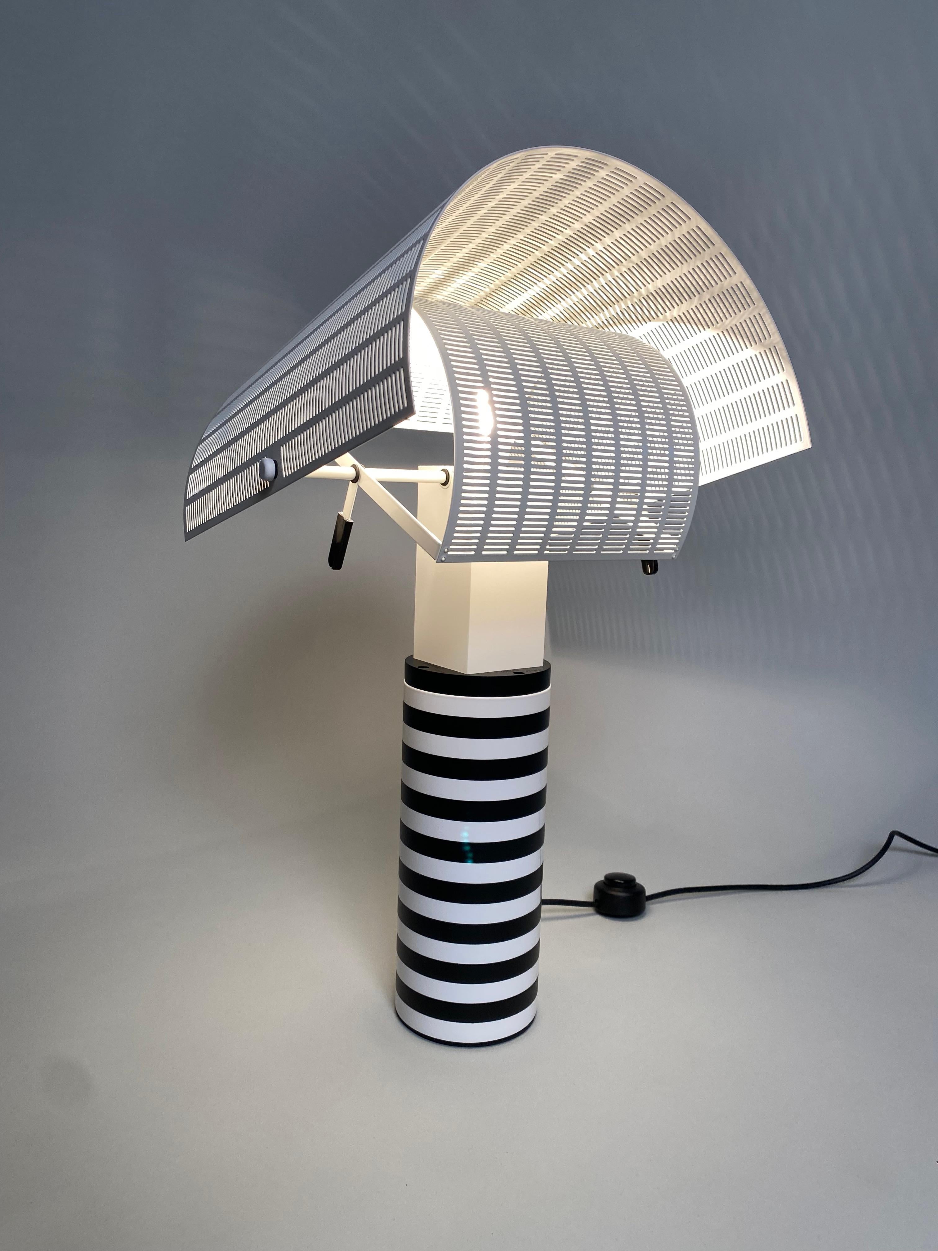 Pareja de lámparas de mesa postmodernas del famoso arquitecto Mario Botta. La pantalla ajustable de metal pintado reproduce el sombrero de los shogunes japoneses, del que toma su nombre, y es realmente práctica para dirigir el haz de luz en la