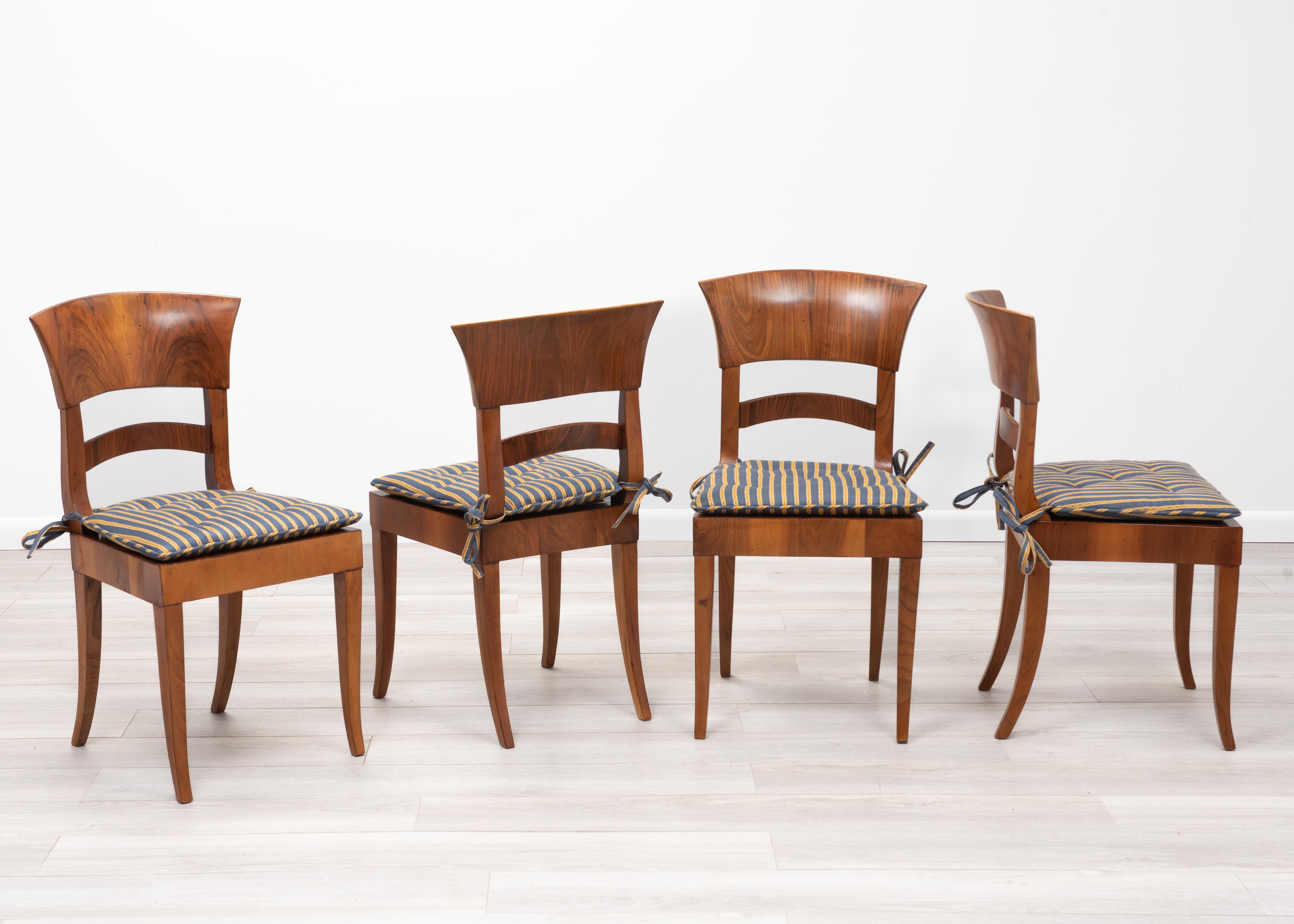 A set of four Mario Buatta Living Biedermeier Style dining or side chairs. Walnut Biedermeier-style chair frames, hand tied cane seats and loose chintz upholstered seat cushions. The chintz cushions are tied to the chair backs with silk ribbon and