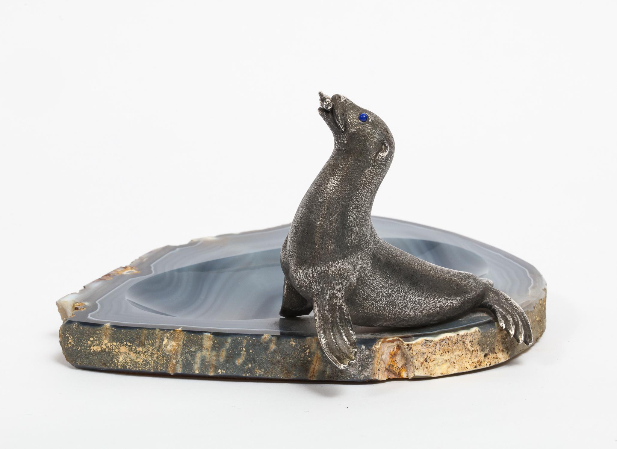 Mario Buccellati,
A rare ashtray or centerpeice with a silver seated seal eating a fish with Lapis Lazuli eyes, mounted on blue agate.

Marked Buccellati, Made in Italy and 800.

The meaning of blue agate is calmness. Blue agate stone is known