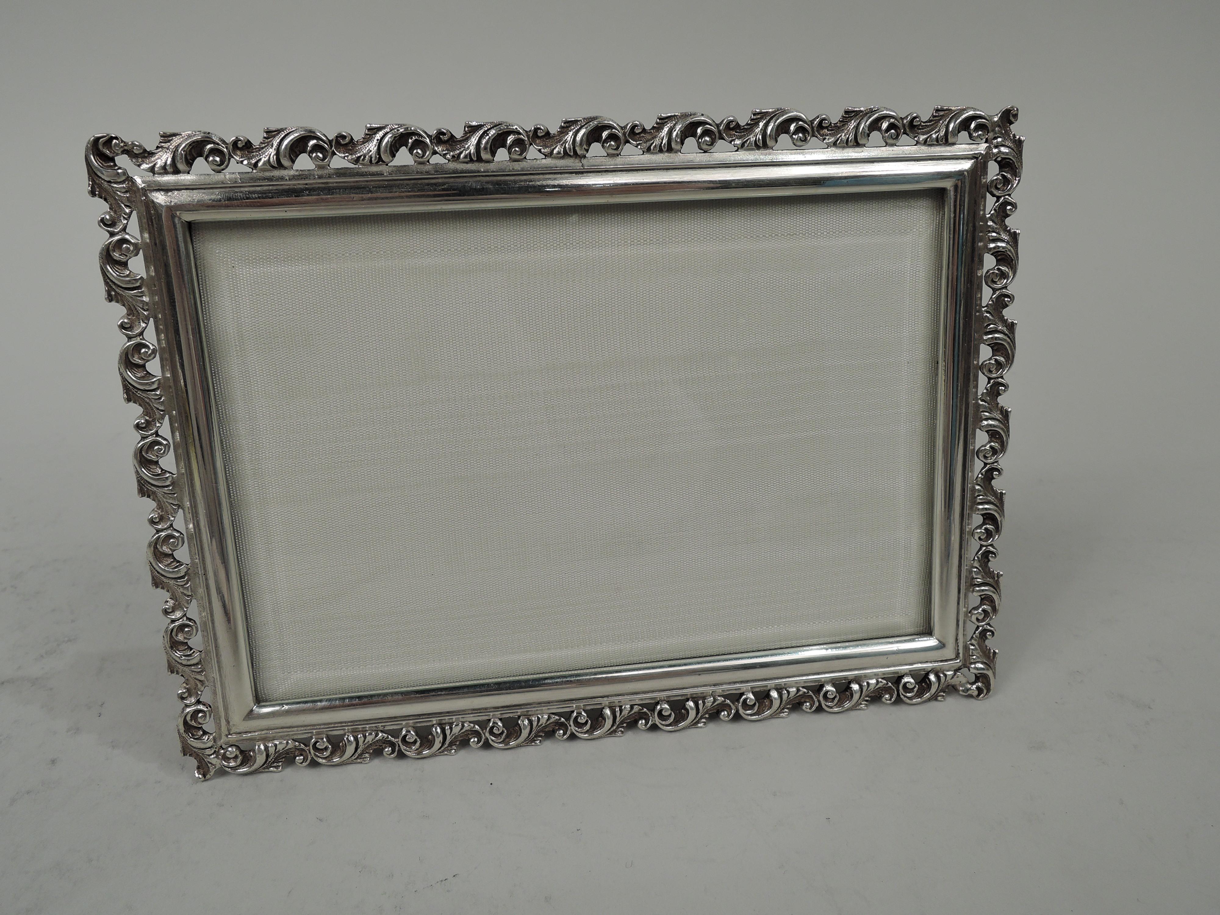 Modern Classical sterling silver picture frame. Made by Mario Buccellati in Italy. Rectangular window in molded surround applied with cast leafing scroll border. Heavy gauge. With beveled glass, silk lining, and chamois back and hinged easel support