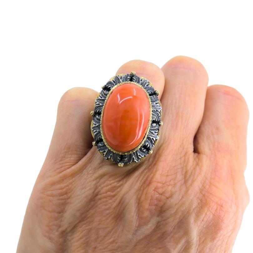 Ein Ring von Mario Buccellati mit Korallenmotiven, gefasst in Silber mit Goldakzenten.
Dieser Buccellati-Ring im Vintage-Stil ist mit einem ovalen Korallen-Cabochon besetzt. Die Koralle ist in Gold gefasst und von einer erhabenen Silbereinfassung