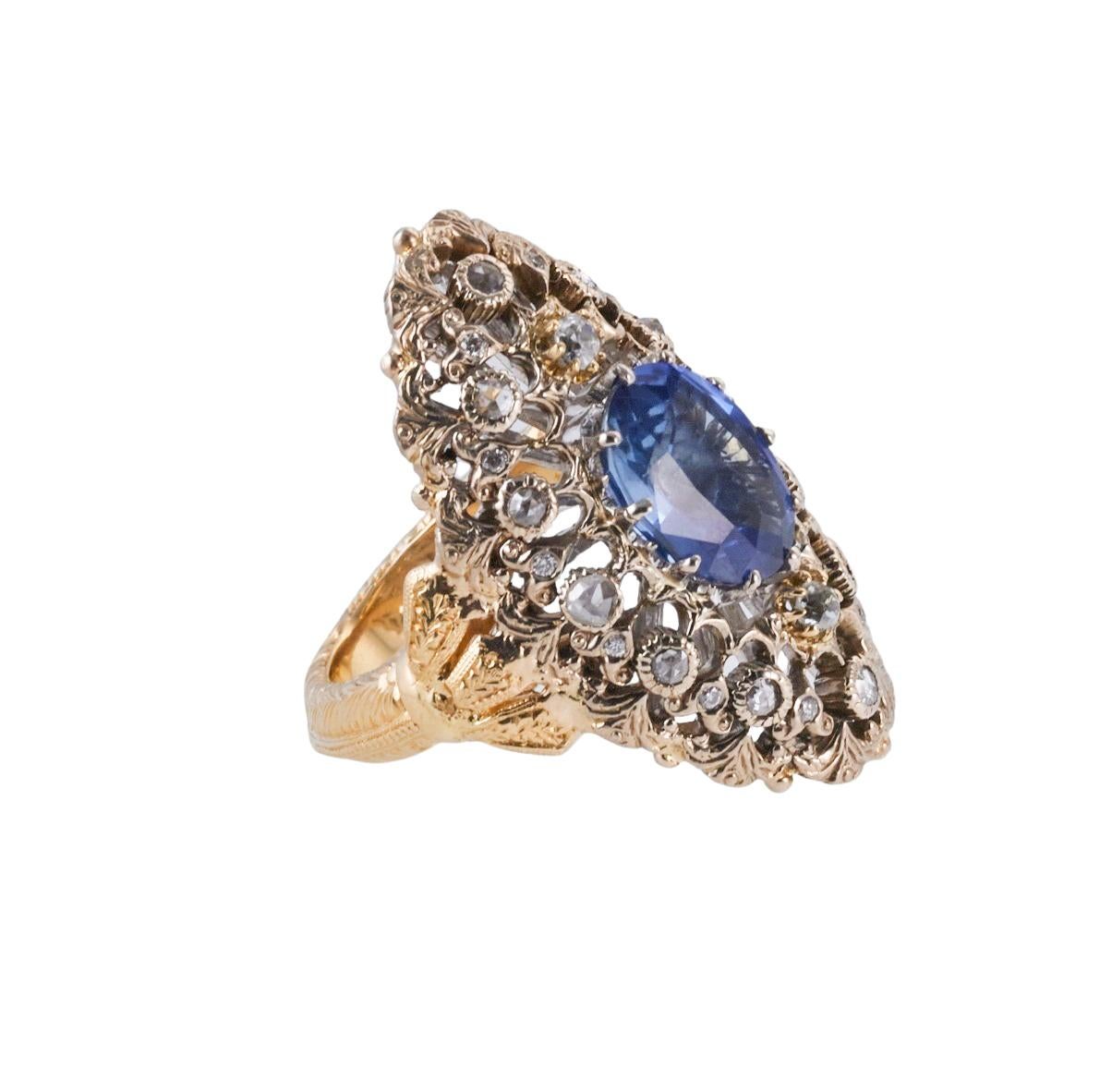 18k white and yellow gold ring by Mario Buccellati, set with center oval blue sapphire ( measures approx. 11 x 8.7mm , as allowed by the setting), surrounded with approx. 0.40ctw in diamonds. Ring size 5.25, top is 33mm x 20mm. Marked M. Buccellati,