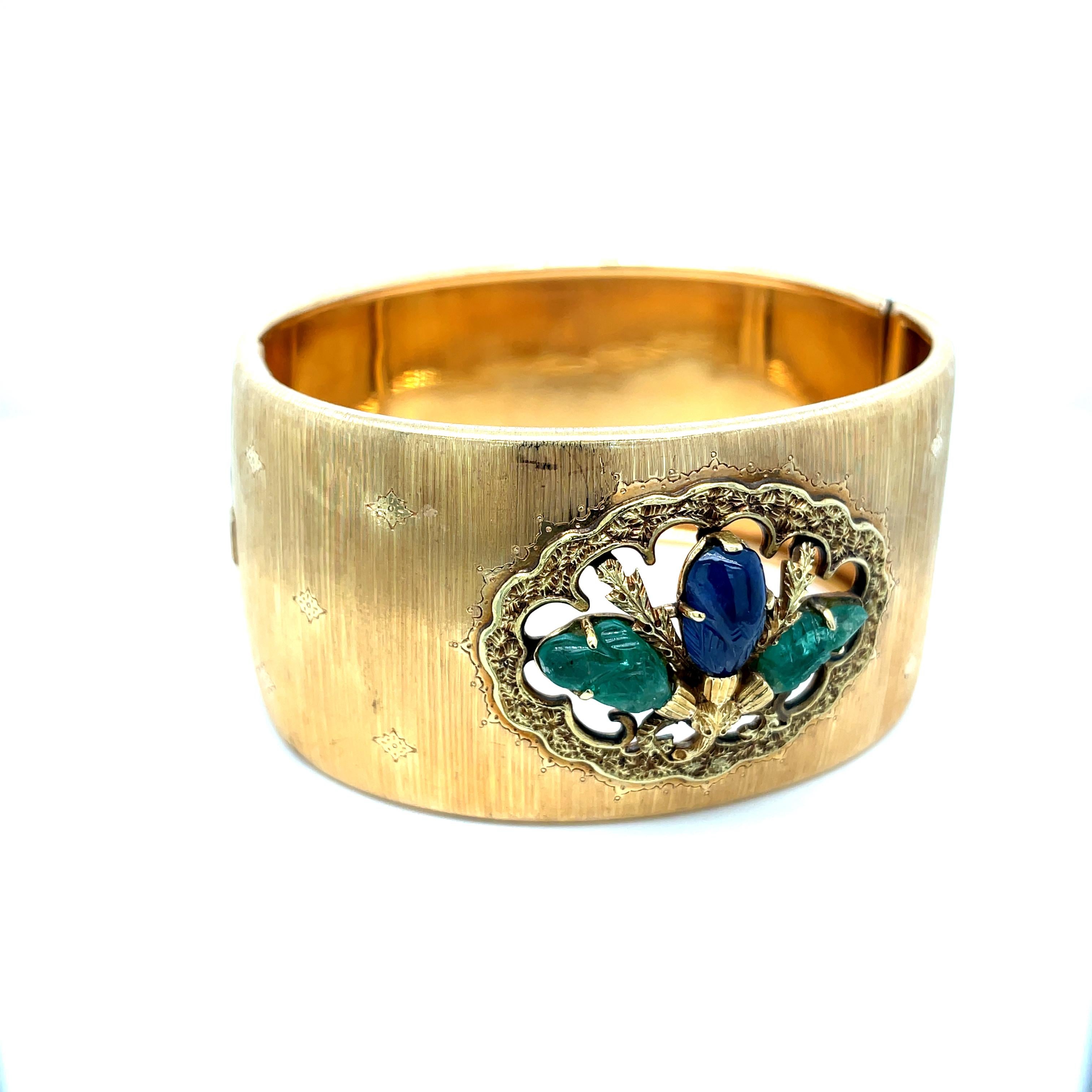 Iconic Mario Buccellati Wide Bracelet in yellow gold set with Tutti Frutti carved natural emeralds and sapphire. 
The rigato effect is obtained by handmade engraving. Small and shiny gold beads play with the opaque texture.
Has a total weight of 62