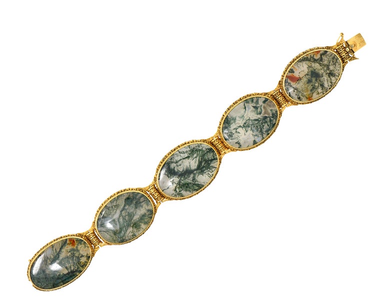 Featuring five oval tablets of moss agate measuring 21.0 x 31.0 mm. Transparent in body color with dark green, orange and white veining. Bezel set in ornately engraved foliate frame surrounds
Hinged to articulate with engraved scroll motif reverse.