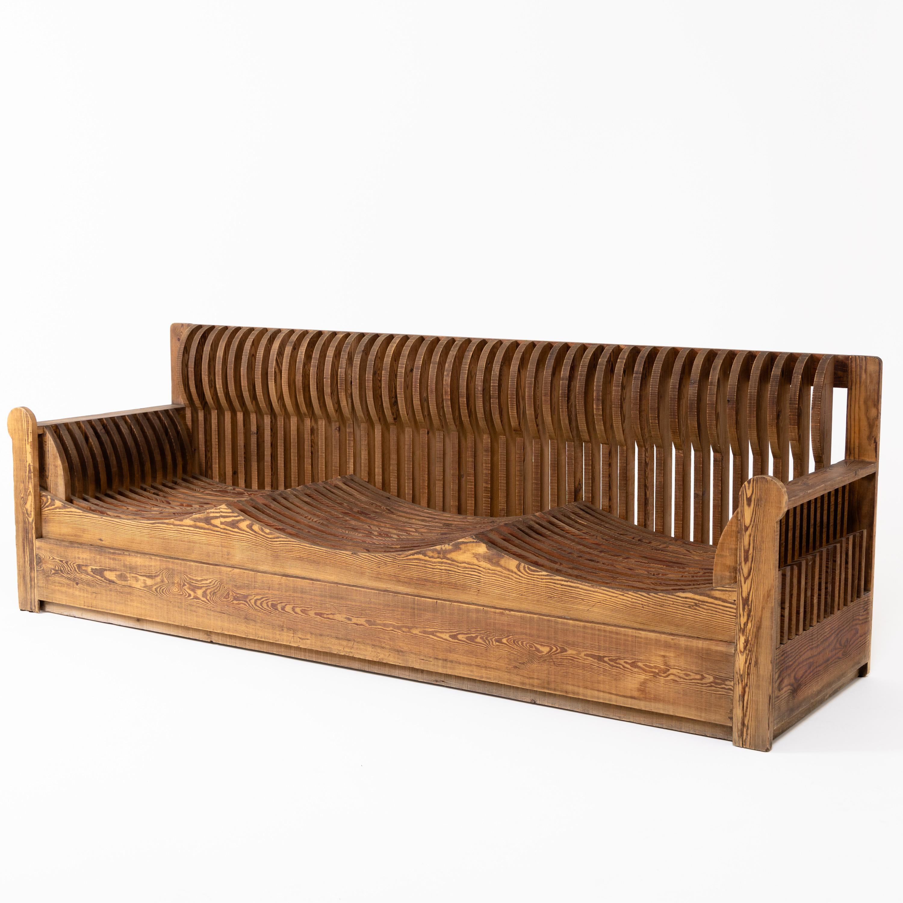 Large three-seat bench in pine of slatted construction with scalloped seat and back. Stamped Ceroli on the side.