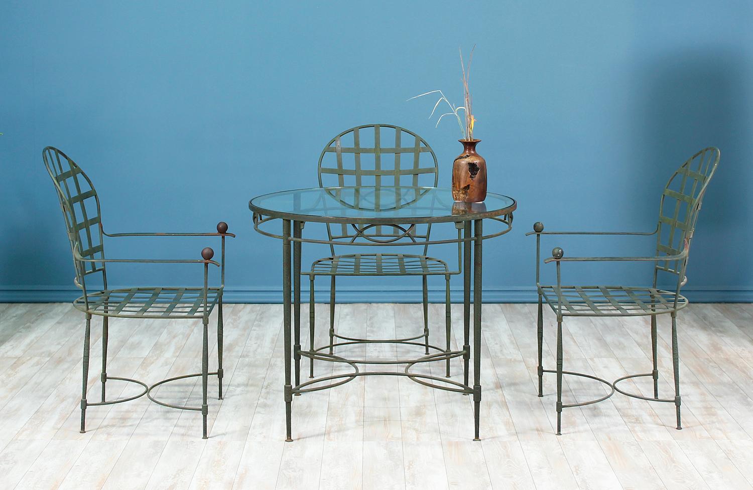 Lovely patio set designed by Mario Papperzini for John Salterini in the United States, circa 1950s. This set features a round glass dining table and a set of four chairs made of hand-hammered iron. The Fine craftsmanship shows a beautiful verdigris