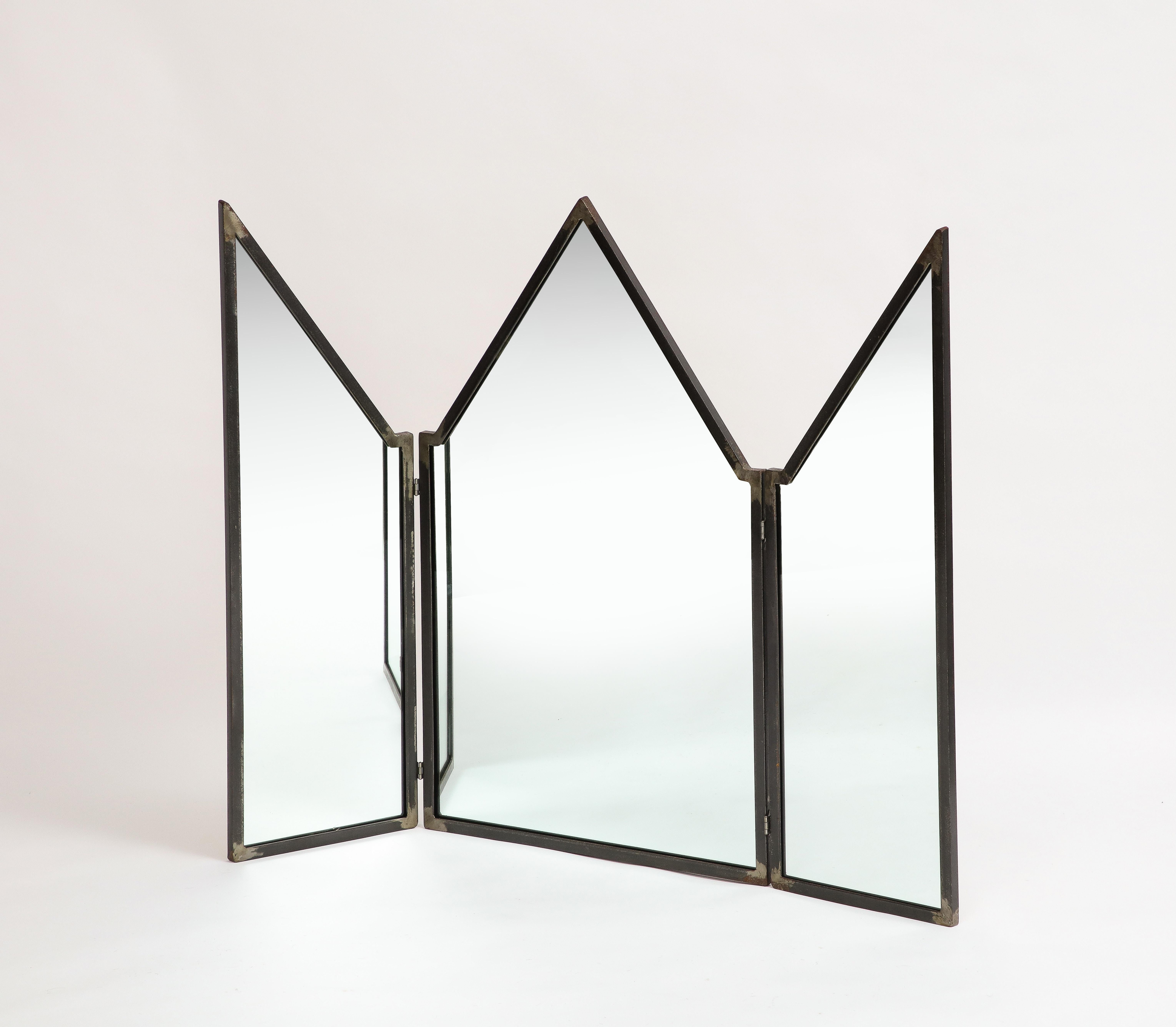 Miroir pliant moderne en fer patiné de Mario Villa (1953-2021), provenant de sa succession. Le miroir est constitué de trois panneaux à fronton avec des sommets en pointe. Le miroir et le support en bois ont été remplacés en 2022. 

Mesures : 39