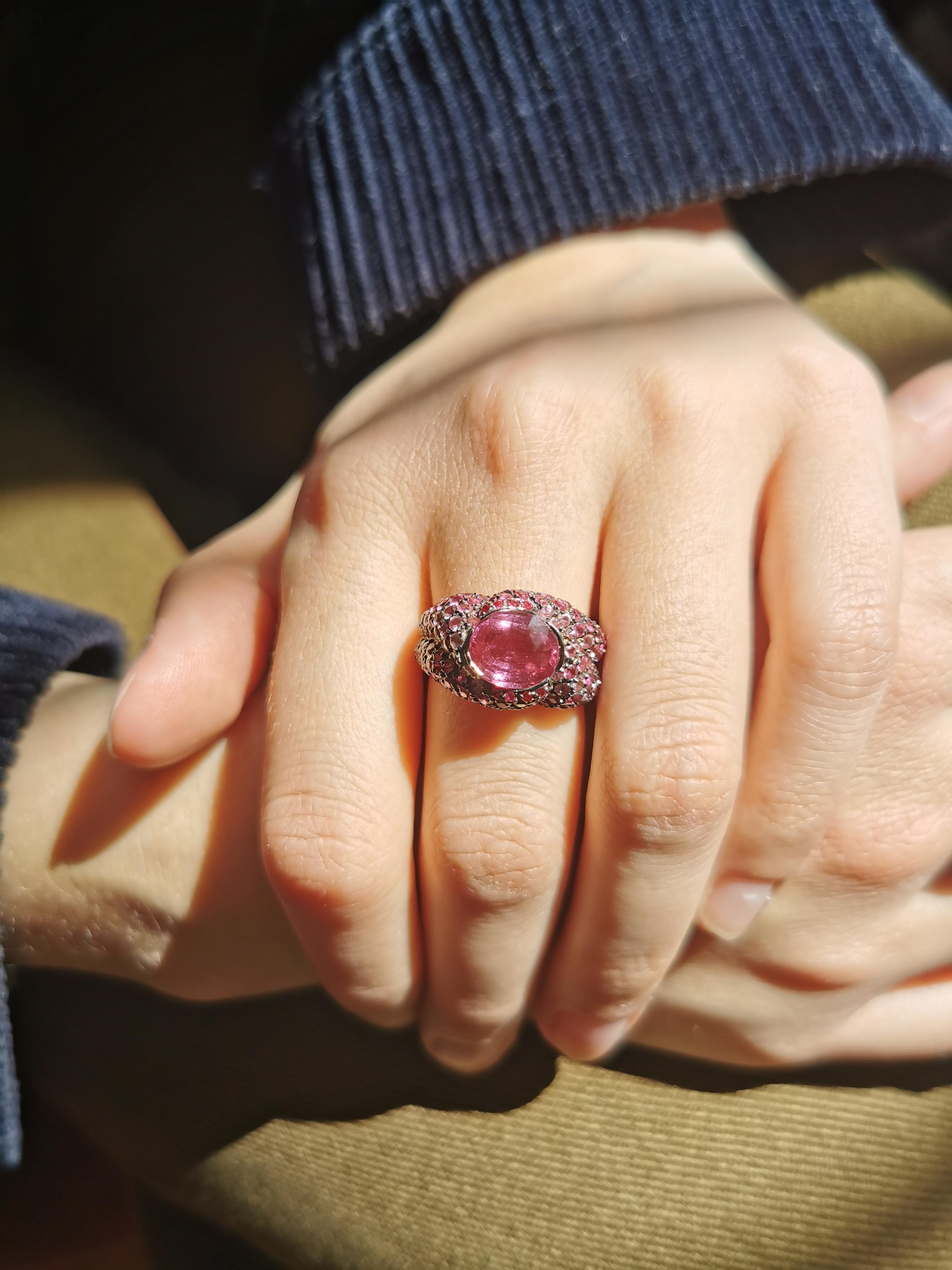A pink sapphire cushion with an intense and glittery colour is enhanced by a subtle paved pink rubies and pink sapphires on the mount. The precious stone's graduation colours accentuates the form and reveals the ring's volume. 
18K White Gold with