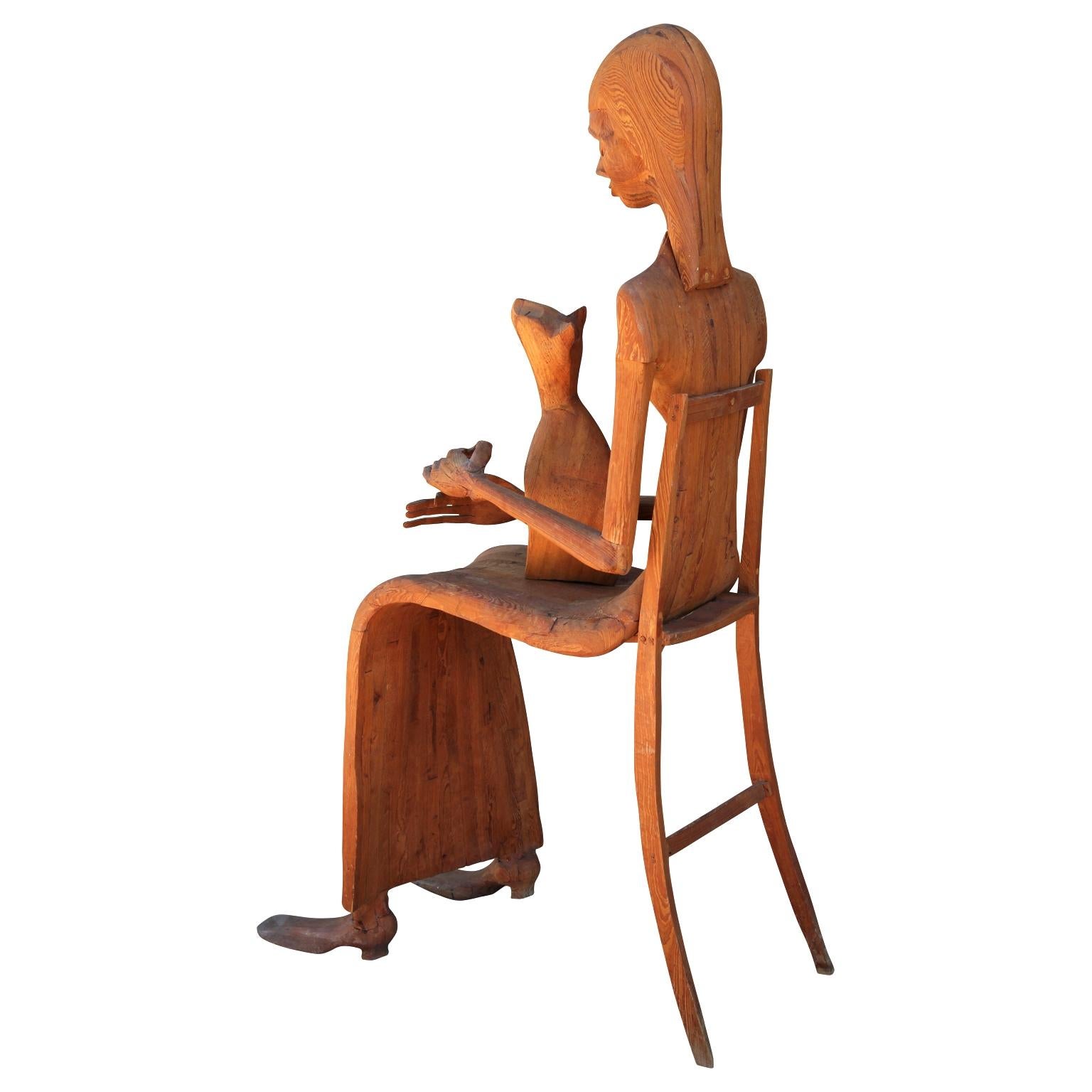 Hand carved wooden sculpture of a seated woman in a chair with a pet cat in her lap. The work features intricately carved facial features, elongated fingers, and the illusion of a separate chair. Created in the style of Marion Perkins, an iconic