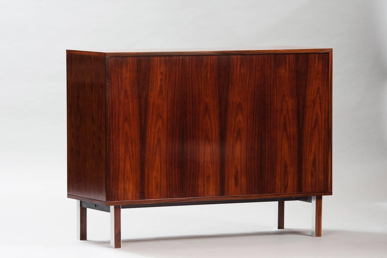 Rosewood cabinet with a tambour door and round metal chrome feet.
    