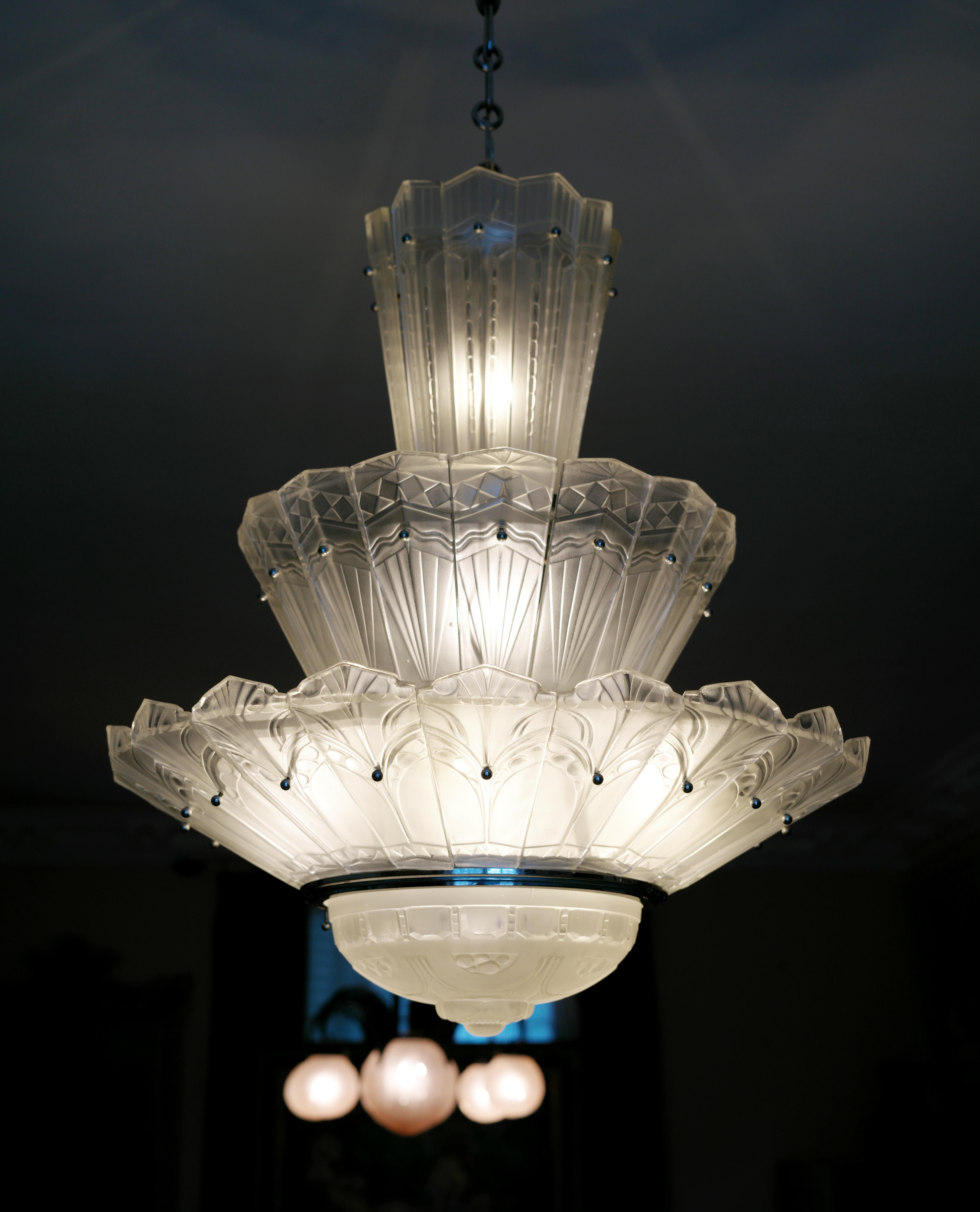 Véritable lustre d'époque en verre Art Déco français de  Marius-Ernest SABINO (Paris), France, années 1930. Grand lustre avec 3 rangées de palmettes en verre et un bol central. Le cadre est en métal chromé. Les rangées sont composées de 20, 16 et 10