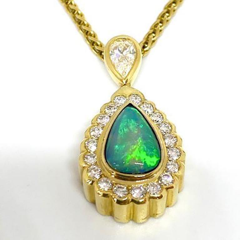 Natural Ethiopian opal and diamond pendant designed by Mark Areias Jewelers in 18K yellow gold. The natural opal is pear cabochon shape and bezel set, surrounded by diamond scalloped edge halo. The bail contains one (1) large pear shape natural