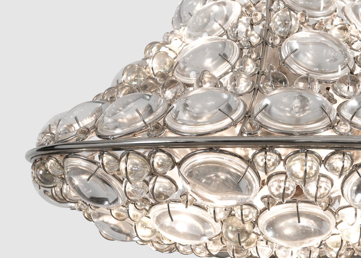 Tzar by Mark Brazier-Jones is a sparkling arrangement of light steel set with a myriad of jewel-like semi-spheres of glass. This remarkable, symmetric cluster of refracting and reflecting elements has such an effect on light as to intimate motion,