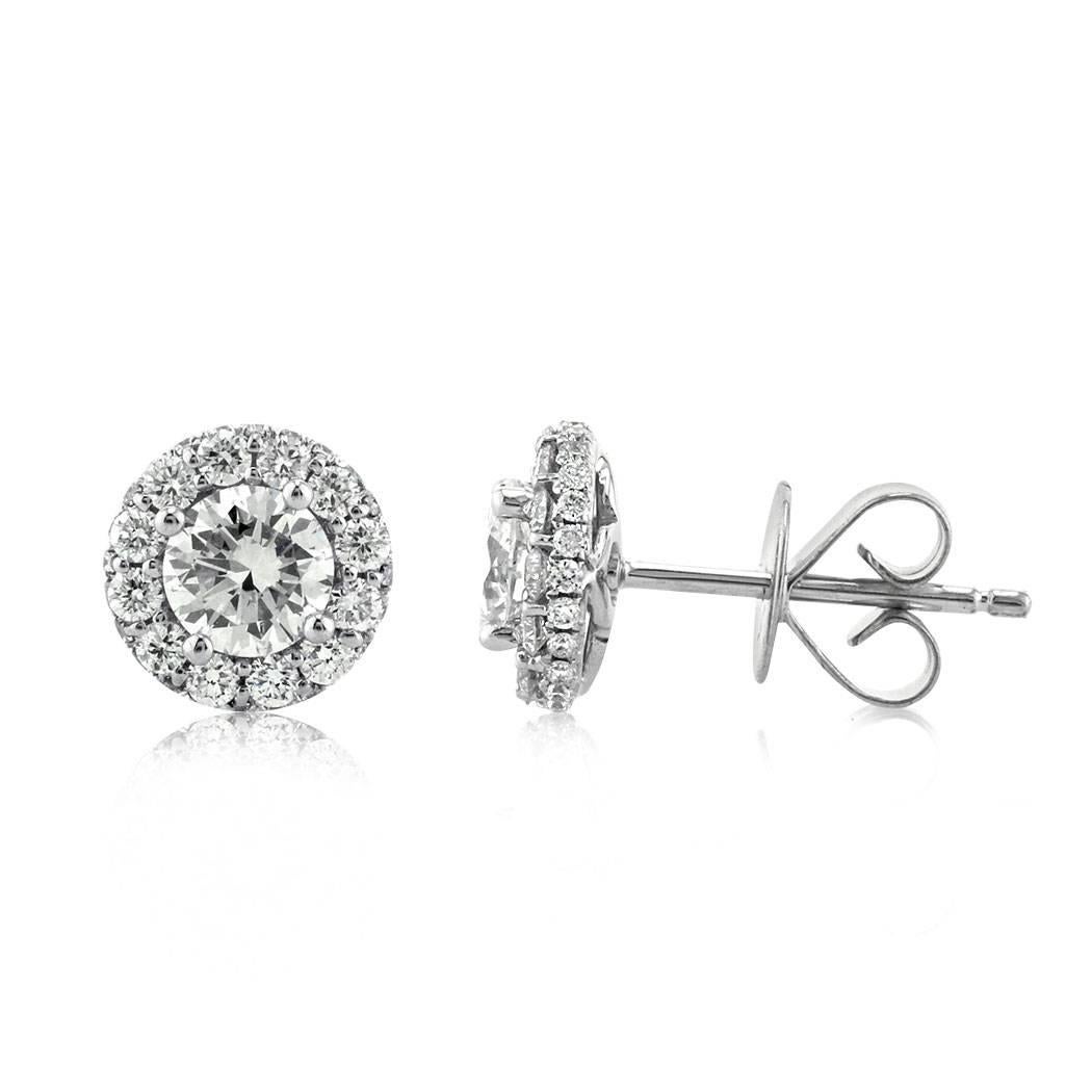 This stunning pair of diamond stud earrings showcases 1.15ct of round brilliant cut diamonds graded at E-F, VS1-VS2. They feature a larger round brilliant cut diamond at the center surrounded by a halo of shimmering diamonds. They are set in a high