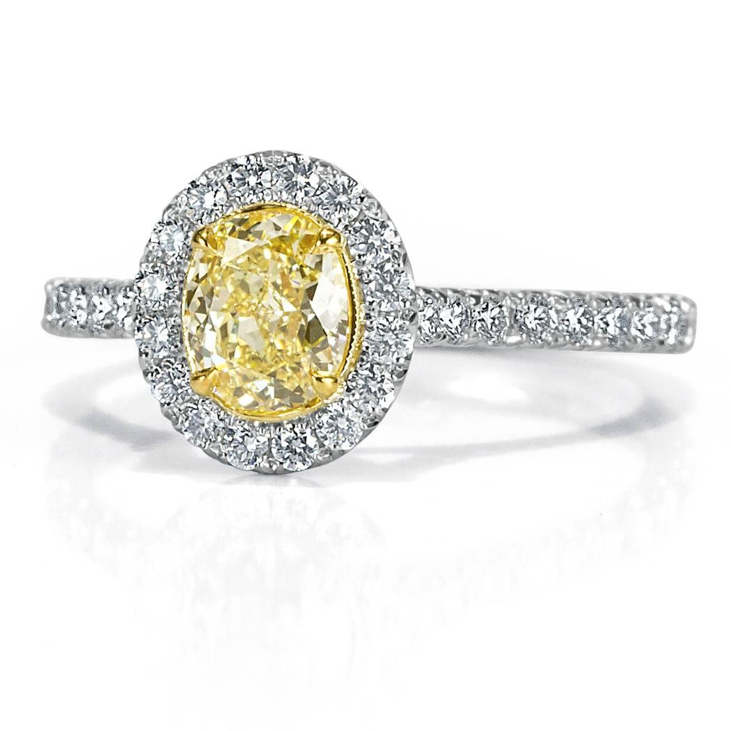 This beautiful diamond engagement ring showcases a lovely 0.70ct oval cut center diamond, GIA certified at Fancy Yellow-VS2. It is surrounded by a halo of white round brilliant cut diamonds and poised atop a dainty platinum shank adorned with