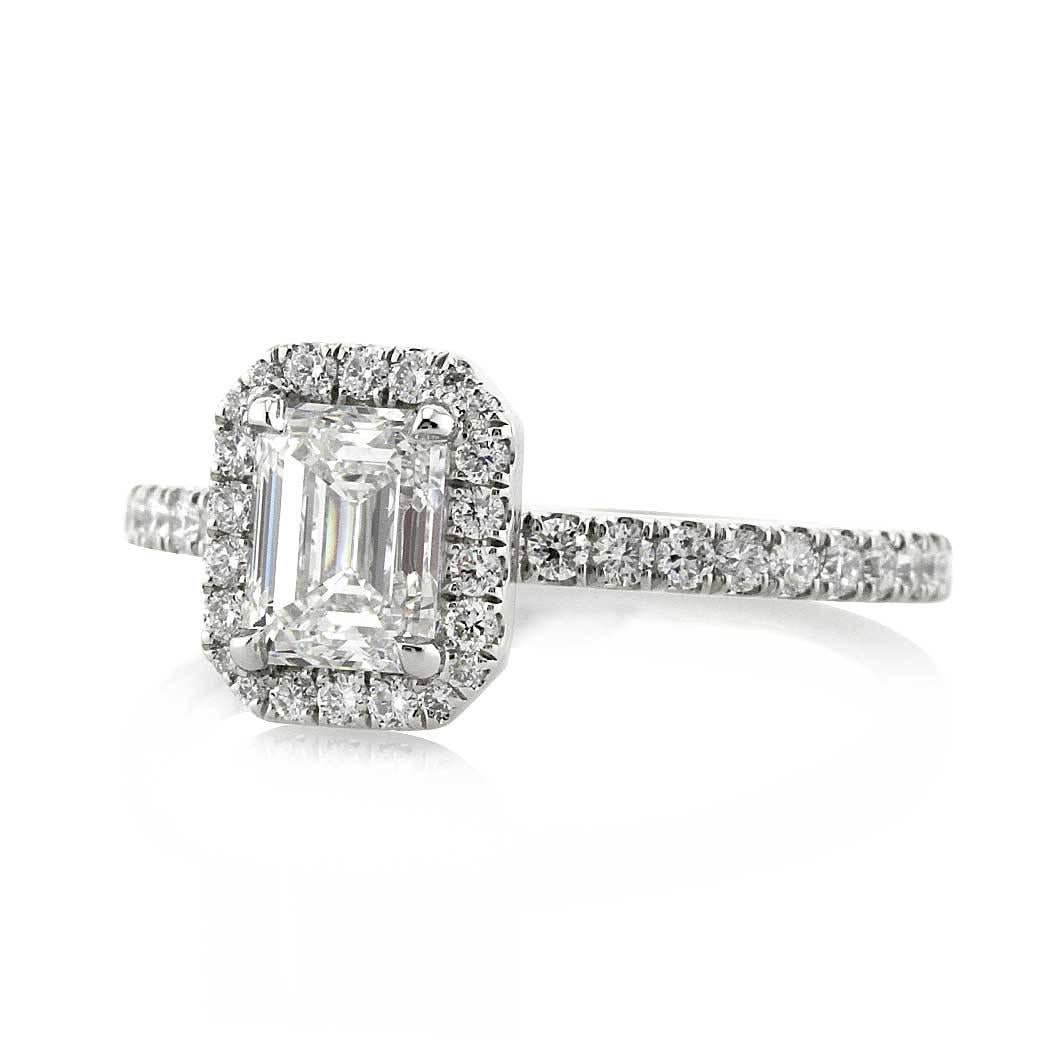 This exquisite emerald cut diamond engagement ring is set with a 1.02ct center diamond, GIA certified at E-VS2. It is accented by a halo of shimmering diamonds as well as one row of round brilliant cut diamonds micro pavé set around the platinum