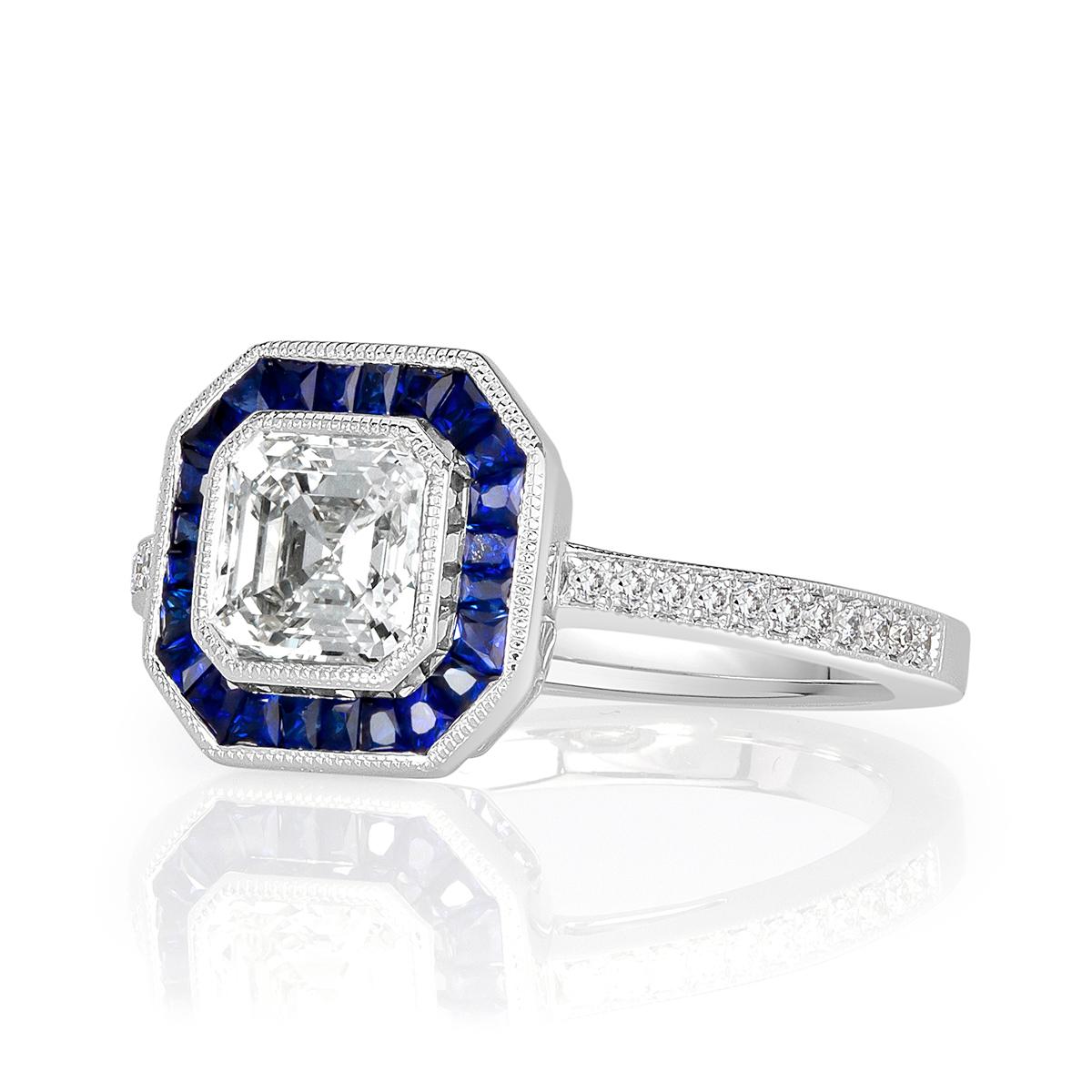 This very unique Asscher cut diamond engagement ring showcases a 1.01ct center diamond, GIA certified at J-VS1. It is bezel set in an 18k white gold center basket featuring hand milgrain detail throughout and accented by a halo of tapered baguette
