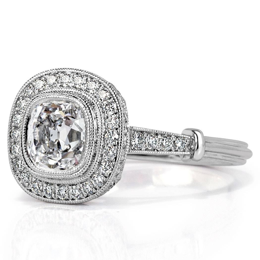 This captivating diamond engagement ring is set with a gorgeous 1.25ct old Mine cut center diamond, GIA certified at D-VS2. It is bezel set in platinum and encased in a two-sided pavé set halo of round brilliant cut diamonds accented with rolled
