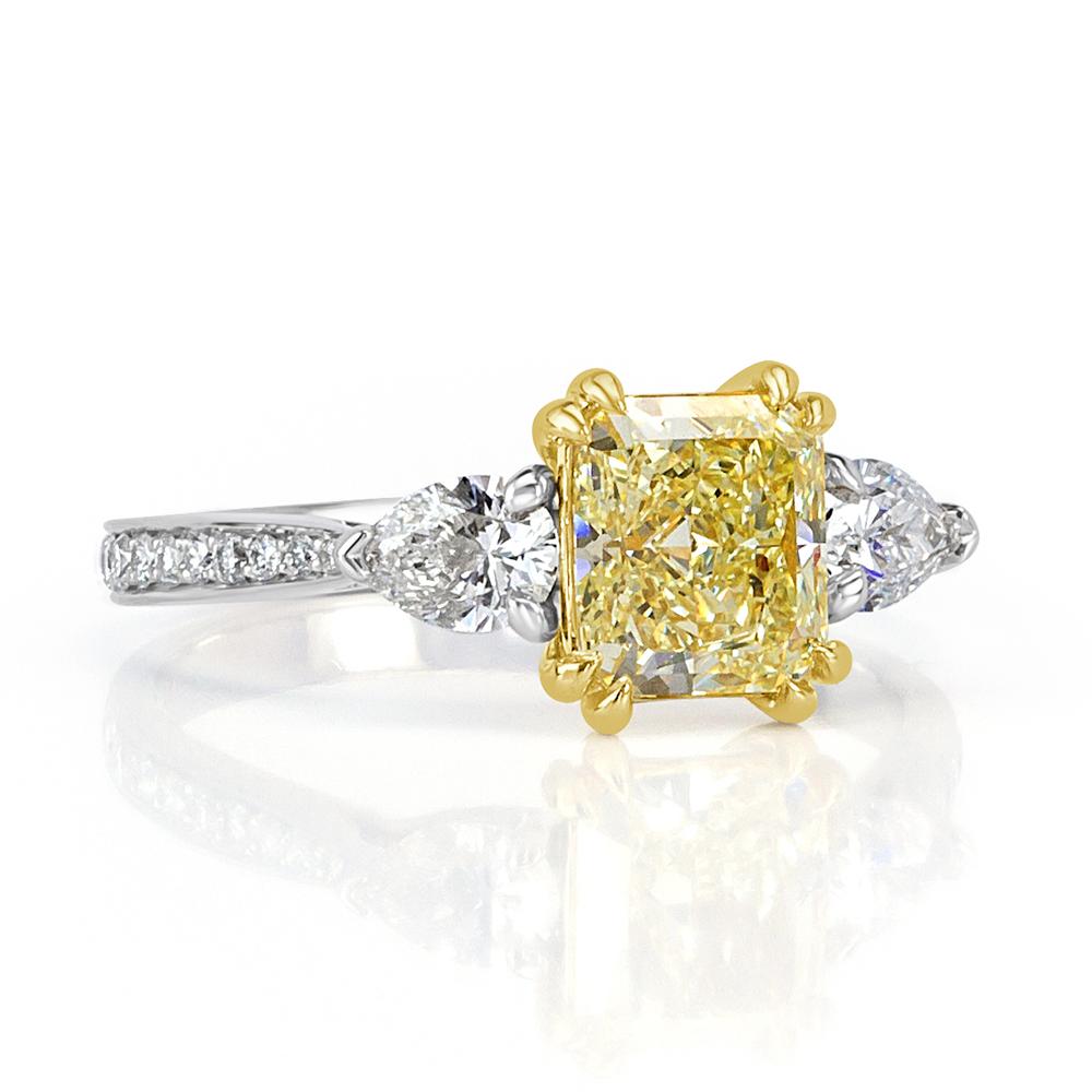 This captivating diamond engagement ring showcases an exquisite 1.25ct radiant cut center diamond, GIA certified at Fancy Light Yellow-VVS1. It is accented by two pear shaped diamonds on either side as well as one row of round brilliant cut diamonds
