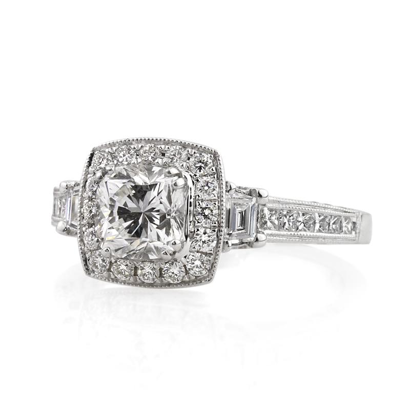 This exquisite diamond engagement ring showcases a unique 1.00ct cushion cut center diamond, GIA certified at G-VS1. It is set in a hand engraved, 18k white gold setting featuring milgrain detail throughout and accented by a dazzling halo of round