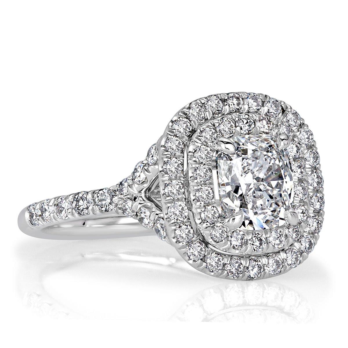 This stunning diamond engagement ring showcases a delightful 1.31ct cushion cut center diamond, GIA certified at E in color, VS1 in clarity. It is encased in a double halo of round brilliant cut diamonds as well as one row of shimmering diamonds set