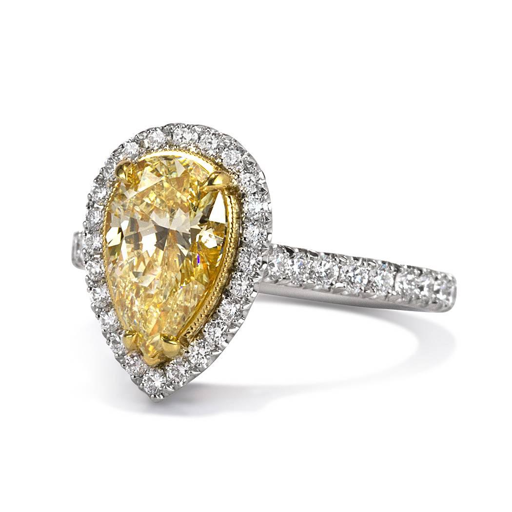 This beautiful diamond engagement ring features a gorgeous 1.77ct pear shaped center diamond, GIA certified at Fancy Yellow-SI2. It is accented by a matching halo of peerless white round brilliant cut diamonds as well as one row of shimmering
