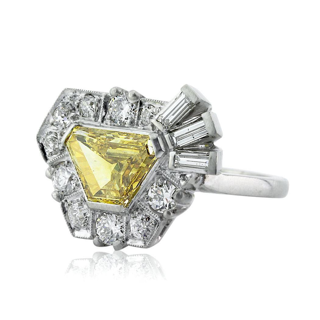 This one of a kind diamond engagement ring is set with a 1.69ct trapezoid center diamond, GIA certified at Fancy Vivid Yellow-I1. It is accented by a unique halo of old European and baguette cut diamonds set atop a high polish platinum shank. The