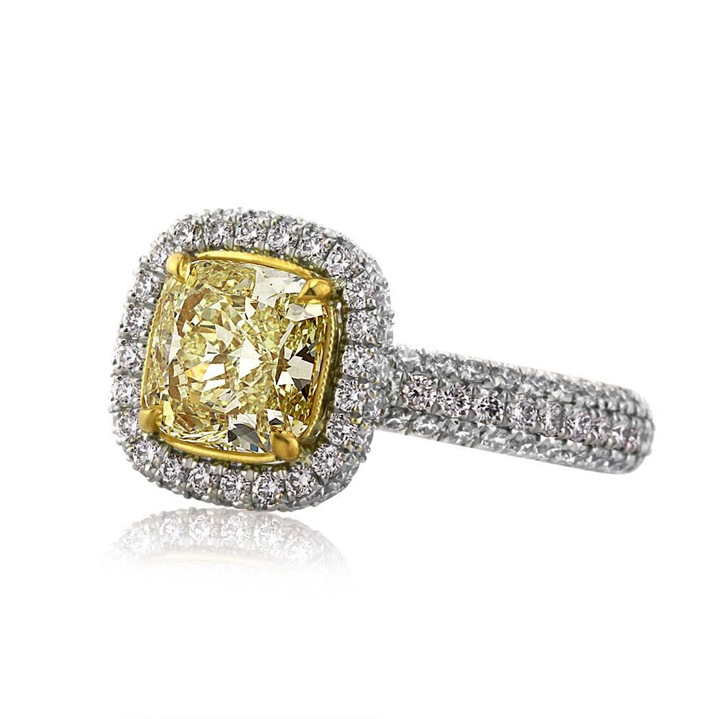 This diamond engagement ring features a 1.66ct cushion cut center diamond, GIA certified at Fancy Intense Yellow-VS1. It is accented by a halo of white round brilliant cut diamonds as well as three rows of shimmering diamonds micro pavé set on all