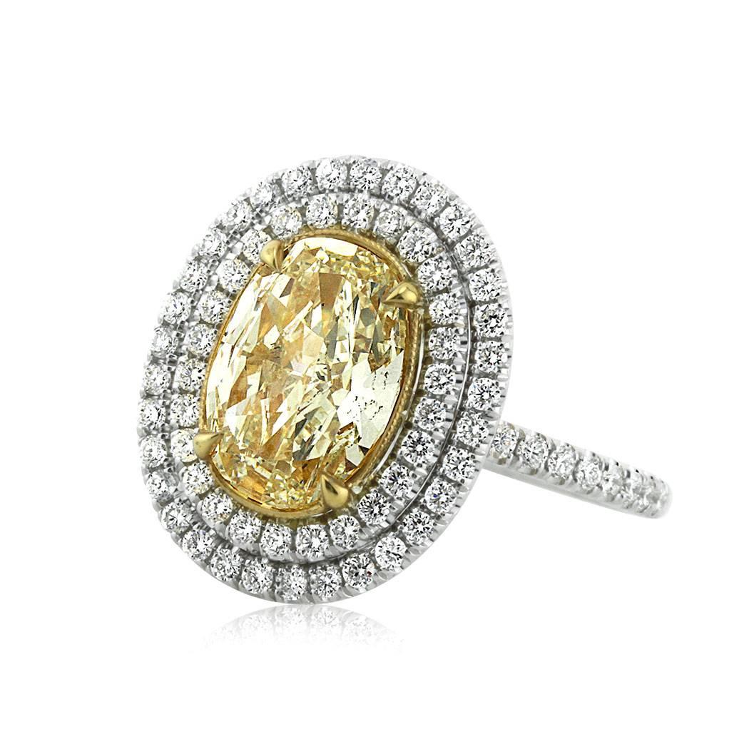 This diamond engagement ring features a 2.15ct oval cut center diamond, GIA certified at Fancy Light Yellow (V)-SI2. It is accented by a double halo of peerless white round brilliant cut diamonds as well as one row of gleaming diamonds micro pavé