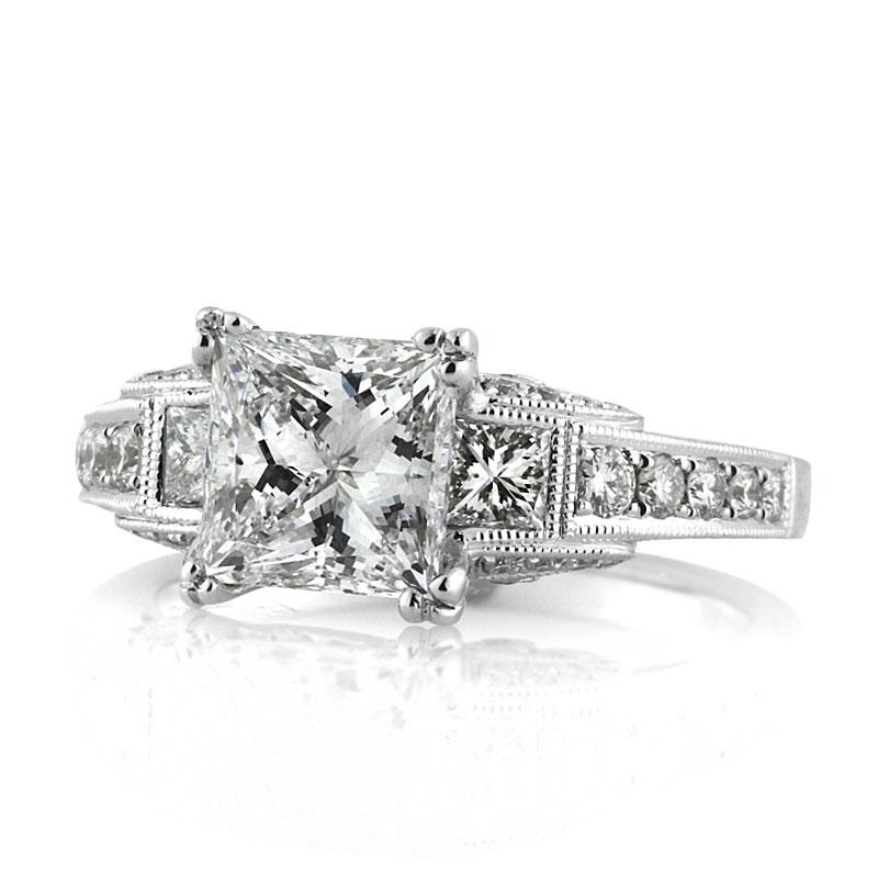 This mesmerizing three-stone diamond engagement ring showcases a gorgeous 2.00ct princess cut center diamond, GIA certified at F in color, VS1 in clarity. It is flanked by two smaller princess cut diamonds bezel set on either side and for maximum