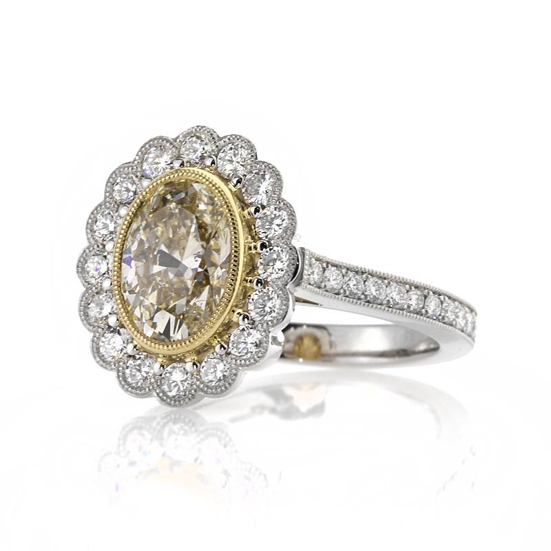 This unique diamond engagement ring features a gorgeous 2.04ct oval cut center diamond, EGL certified at Fancy Yellow-SI2. It is bezel set in a yellow gold center basket featuring delicate milgrain detail throughout and accented by a matching halo