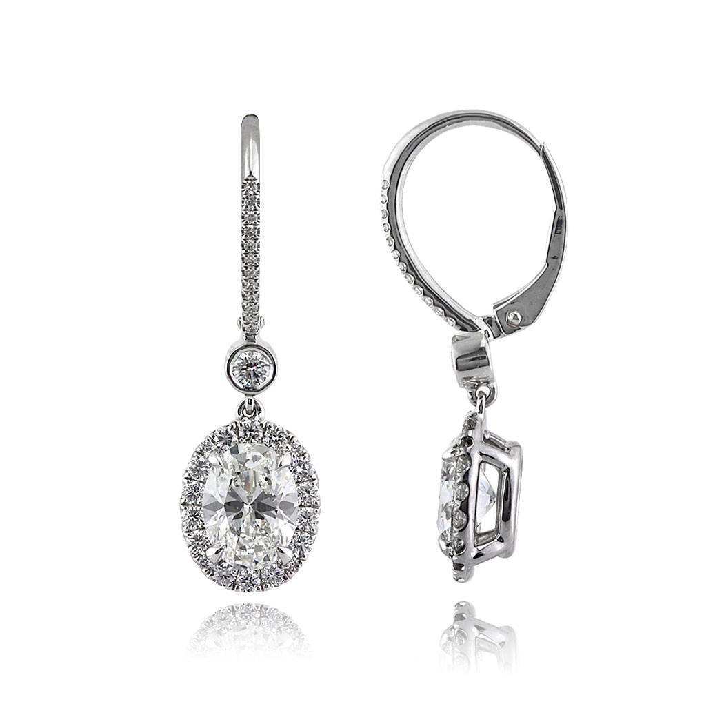 This gorgeous pair of diamond earrings features two gorgeous oval cut diamonds with a total weight of 2.40ct, GIA certified at H-VS2 and H-VVS2. They hang from a bezel set round diamond and are each accented by a halo of shimmering diamonds. For