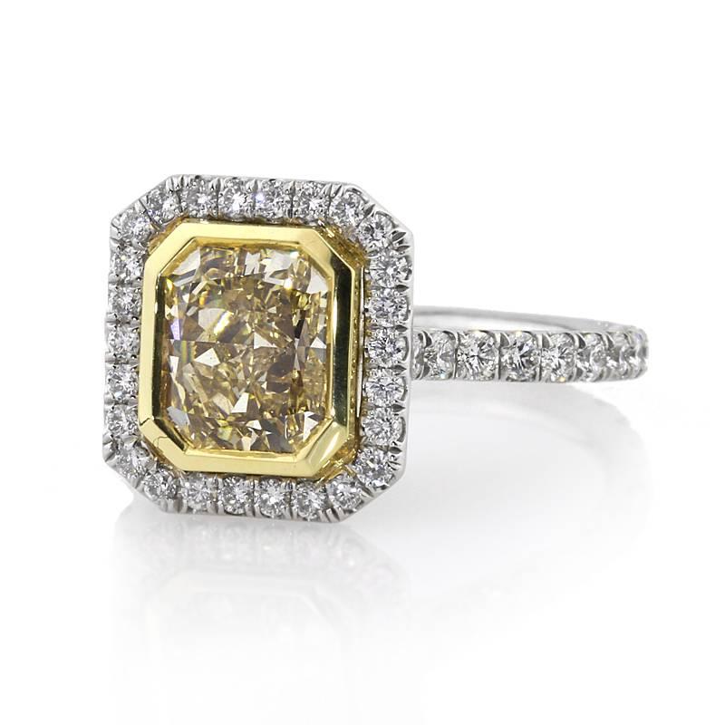 This one of a kind diamond engagement ring showcases a stunning 2.02ct radiant cut center diamond, EGL certified at Fancy Yellow-VS1. It is bezel set in a yellow gold center basket with one row of white round brilliant cut diamonds surrounding it.