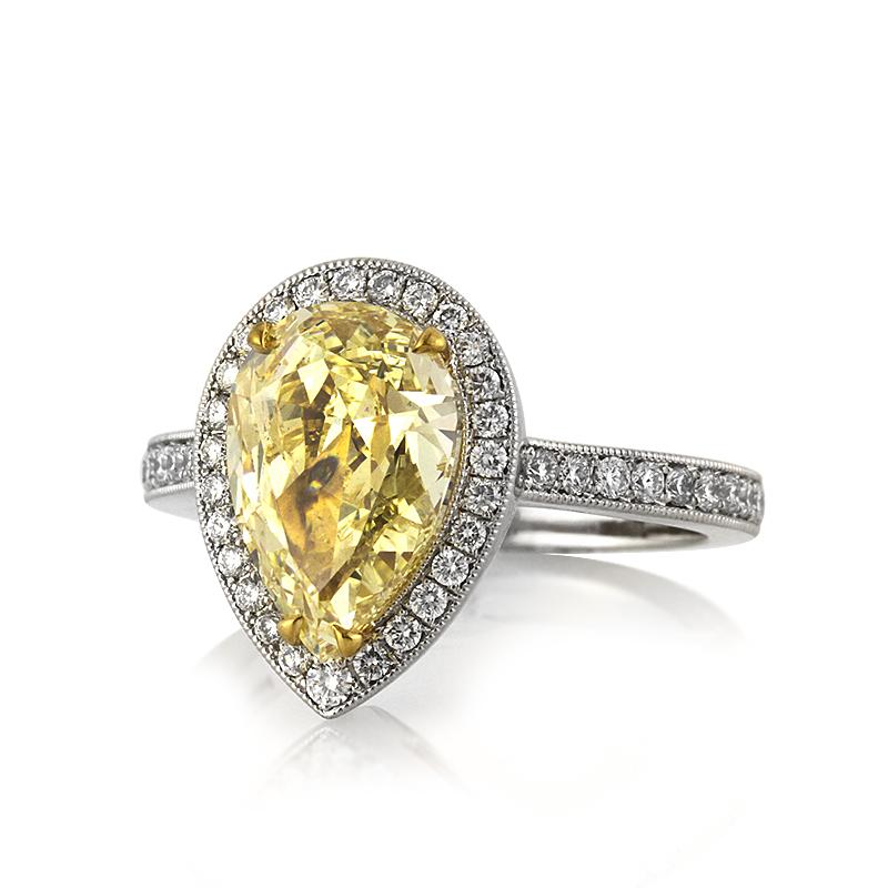 This captivating diamond engagement ring showcases a superb 3.08ct pear shaped center diamond, GIA certified at fancy light yellow-I1. It is complimented by a matching halo of white, round brilliant cut diamonds as well as one row of shimmering