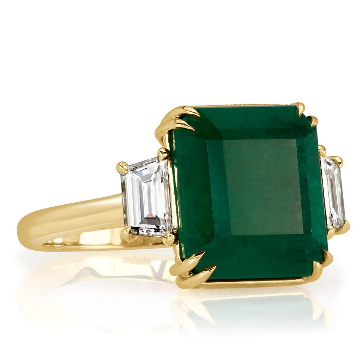 Custom created in 18k yellow gold, this gorgeous emerald and diamond ring showcases a stunning 7.86ct, GIA certified emerald center gemstone. It is secured by sharp eagle claw, double prongs and flanked by two smaller trapezoid cut diamonds on