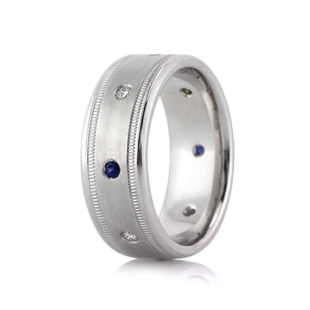 Handcrafted in 14k white gold, this handsome diamond and sapphire men's wedding band showcases 0.35ct of diamonds and blue sapphires alternating around the band. The center of the band is designed in a satin finish and accented with milgrain detail
