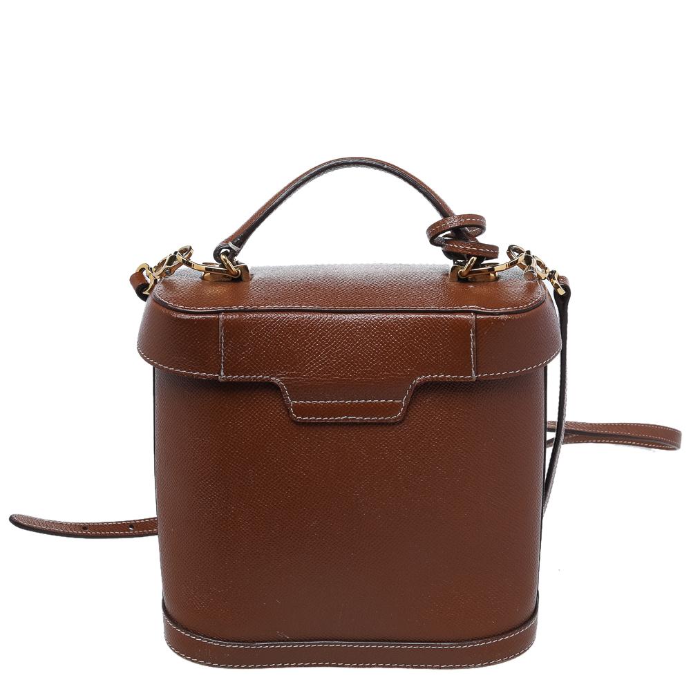 This Mark Cross bag brings a compact size and a luxe style. This multipurpose leather bag would go perfectly for any occasion. It has a structured shape with a top that resembles a lid. The brown-hued bag is held by a top handle and a shoulder