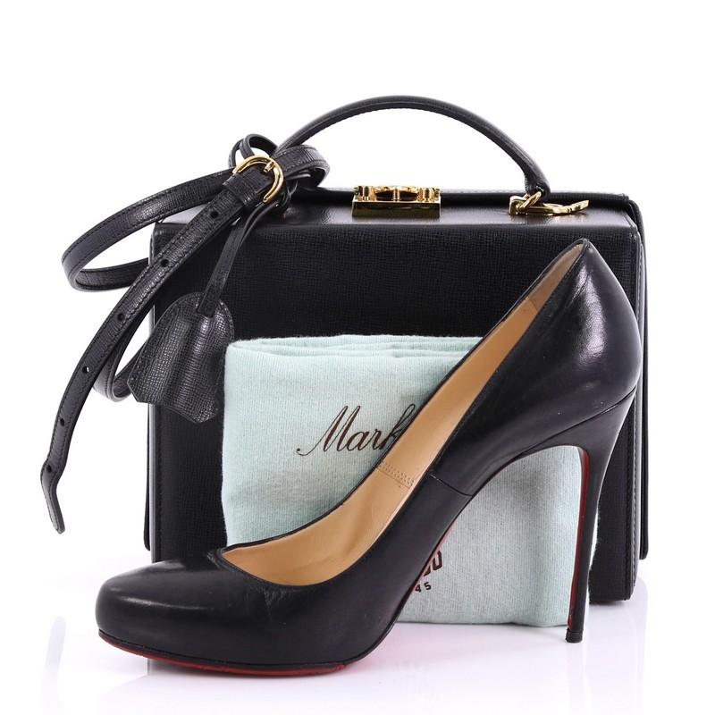 This Mark Cross Grace Box Bag Leather Large, crafted from black leather, features a leather top handle, protective base studs, and gold-tone hardware. Its push-lock closure opens to a red leather interior with zip pocket. **Note: Shoe photographed