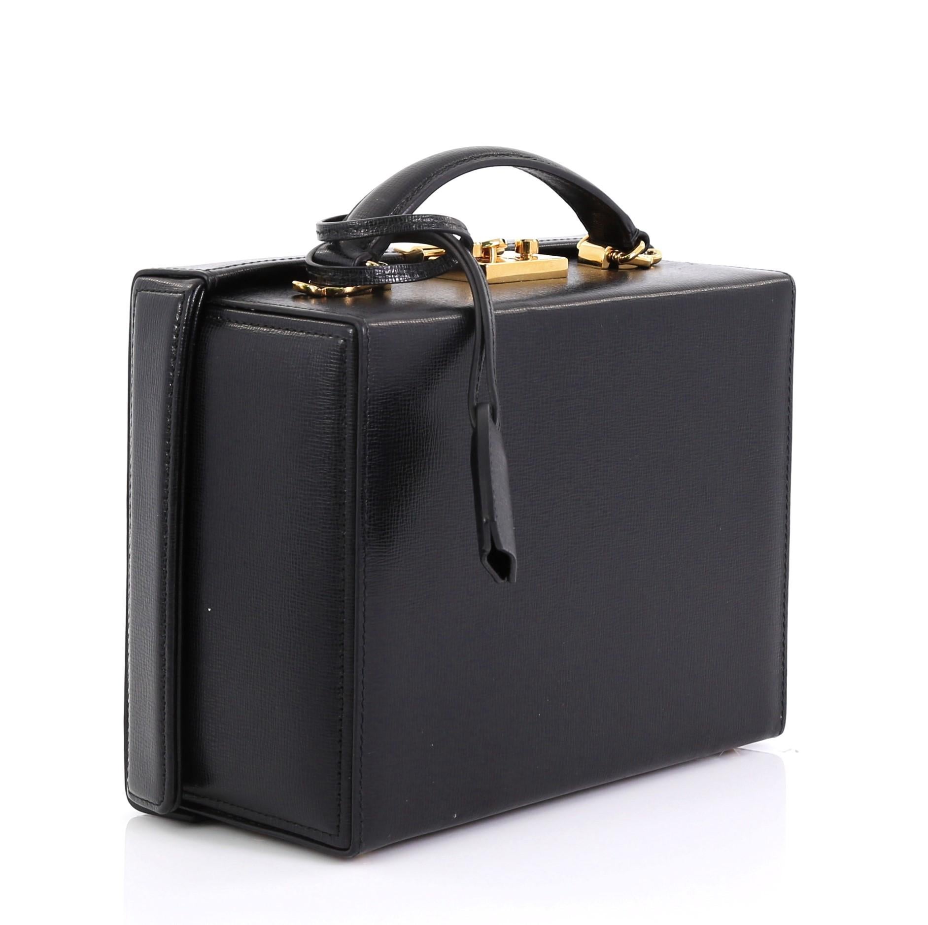 This Mark Cross Grace Box Bag Leather Large, crafted from black leather, features a leather top handle, protective base studs, and gold-tone hardware. Its push-lock closure opens to a red leather interior with zip pocket. 

Estimated Retail Price: