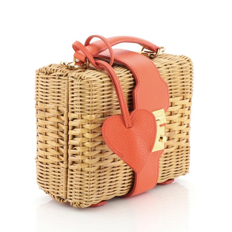 This Mark Cross Harley Bag Rattan Wicker Small, crafted from neutral wicker and orange leather, features a leather top handle, protective base studs, and gold-tone hardware. Its push-lock closure opens to a red fabric interior with slip pocket.