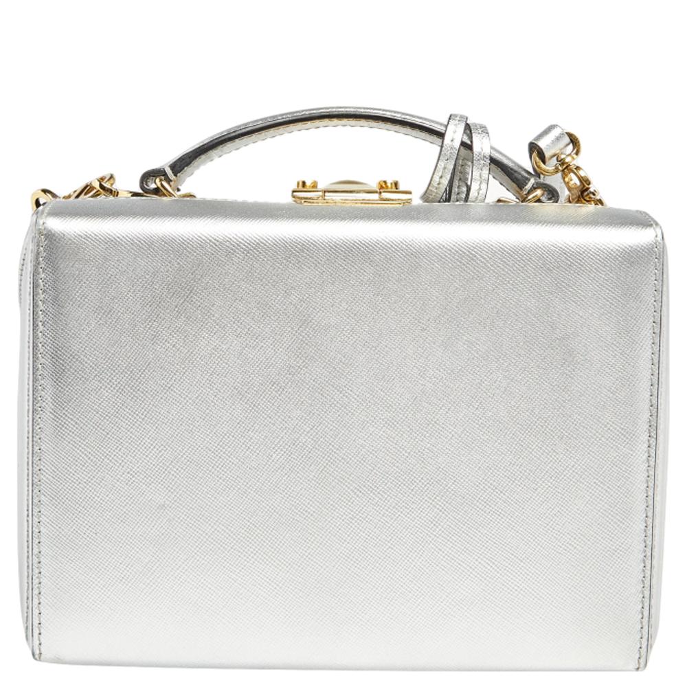 This small Grace Box bag is a statement-making creation you'll love to own! This elegant bag from Mark Cross features a silver leather exterior, a top handle, and gold-toned metal closure on which the brand logo is engraved. This bag is eternally