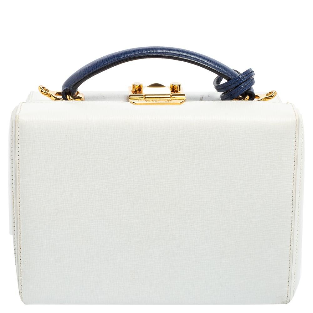 This small Grace Box bag is a statement-making creation you'll love to own! This elegant bag from Mark Cross features a white leather exterior, a blue top handle, and gold-toned metal closure on which the brand logo is engraved. This bag is
