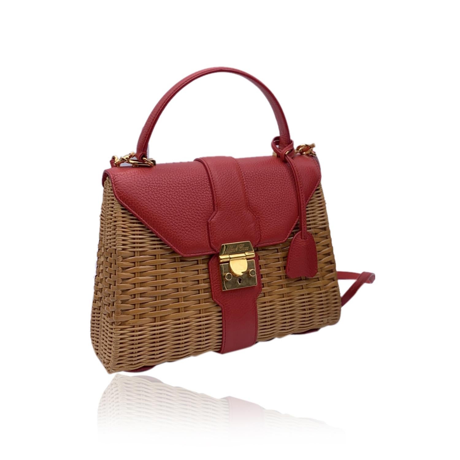 Mark Cross handwoven wicker/rattan satchel detailed with and leather satchel. Flap with push-lock closure. Adjustable and removable shoulder strap. Red fabric lining. Single interior slip and zip pocket. Gold-plated brass