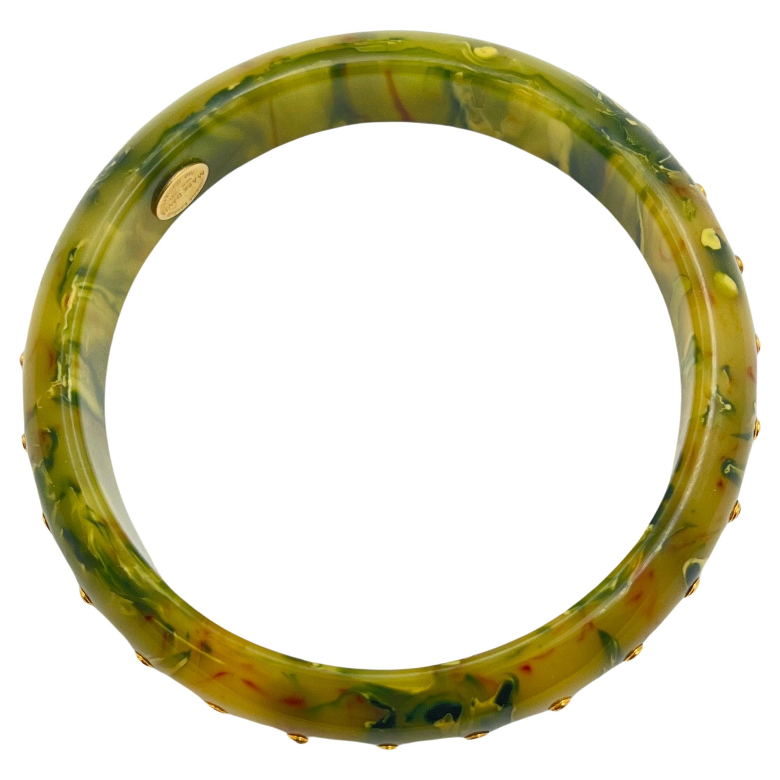 Crafted from vintage bakelite, this Mark Davis bangle bracelet features a swirling pattern of yellow and green, with specks of amber hues.  The bangle is accented by a central row of round brilliant-cut diamonds, peridot, and sapphires.  Each gem is
