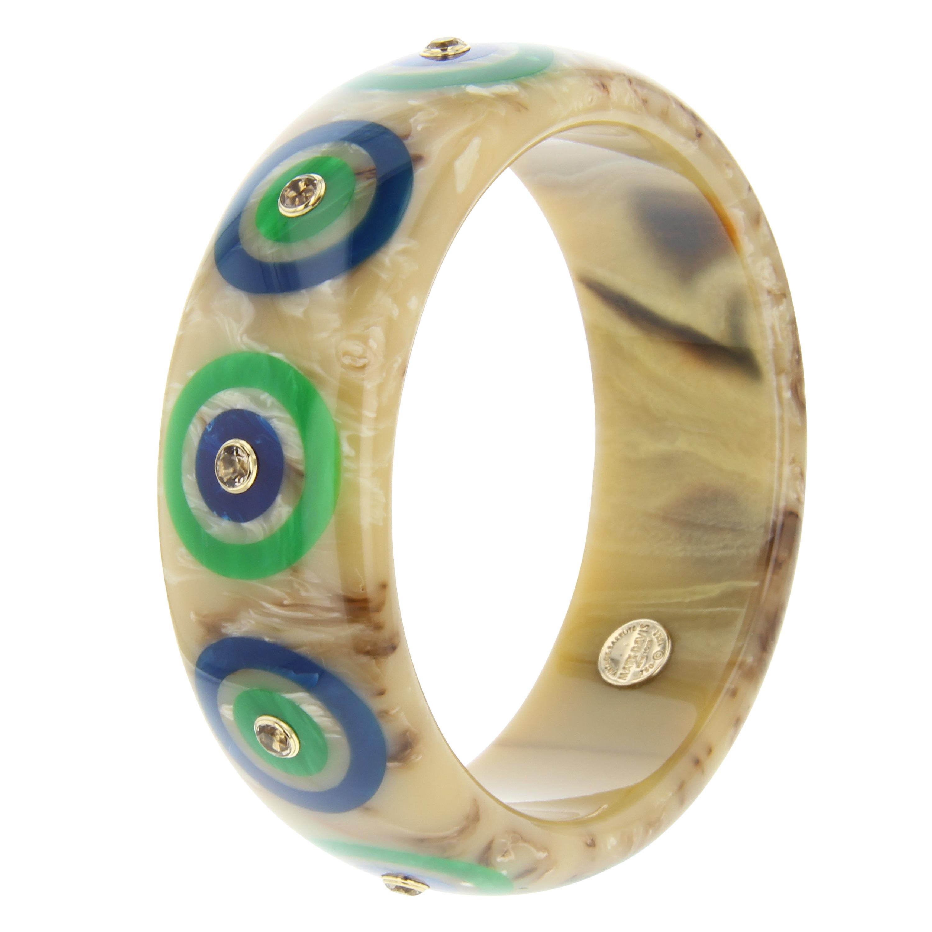 This striking Mark Davis bangle is narrow but still a substantial piece. Beautiful beige bakelite with a very subtle greenish tint has been inlaid with a bullseye pattern of green and blue bakelite. The center of each bullseye is set with smoky