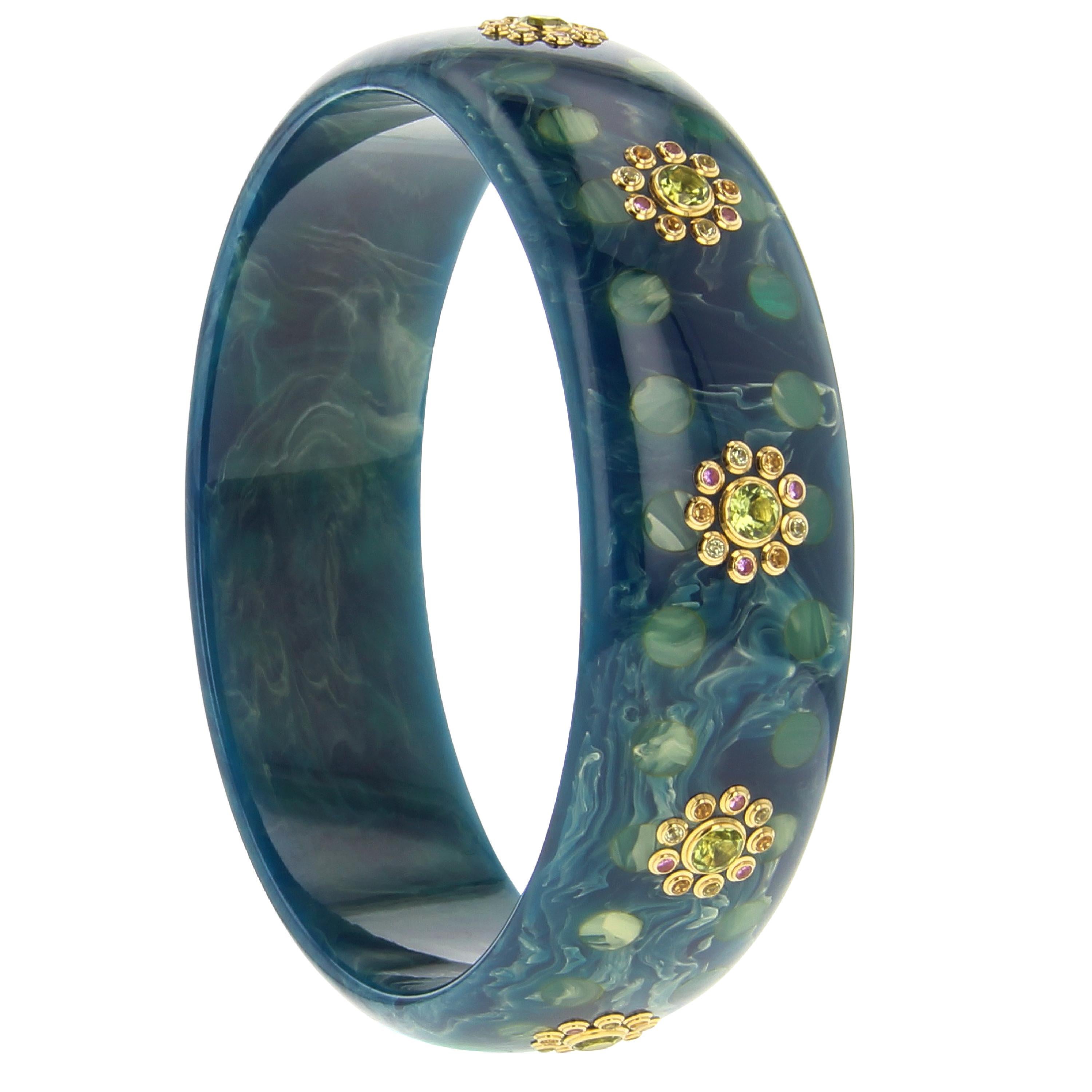 This Mark Davis bangle was made from a beautiful marbled blue bakelite inlaid with a tonal polka dot pattern. Evenly spaced clusters of gemstones circle the bangle. Each cluster is comprised of a central peridot surrounded by smaller peridot,
