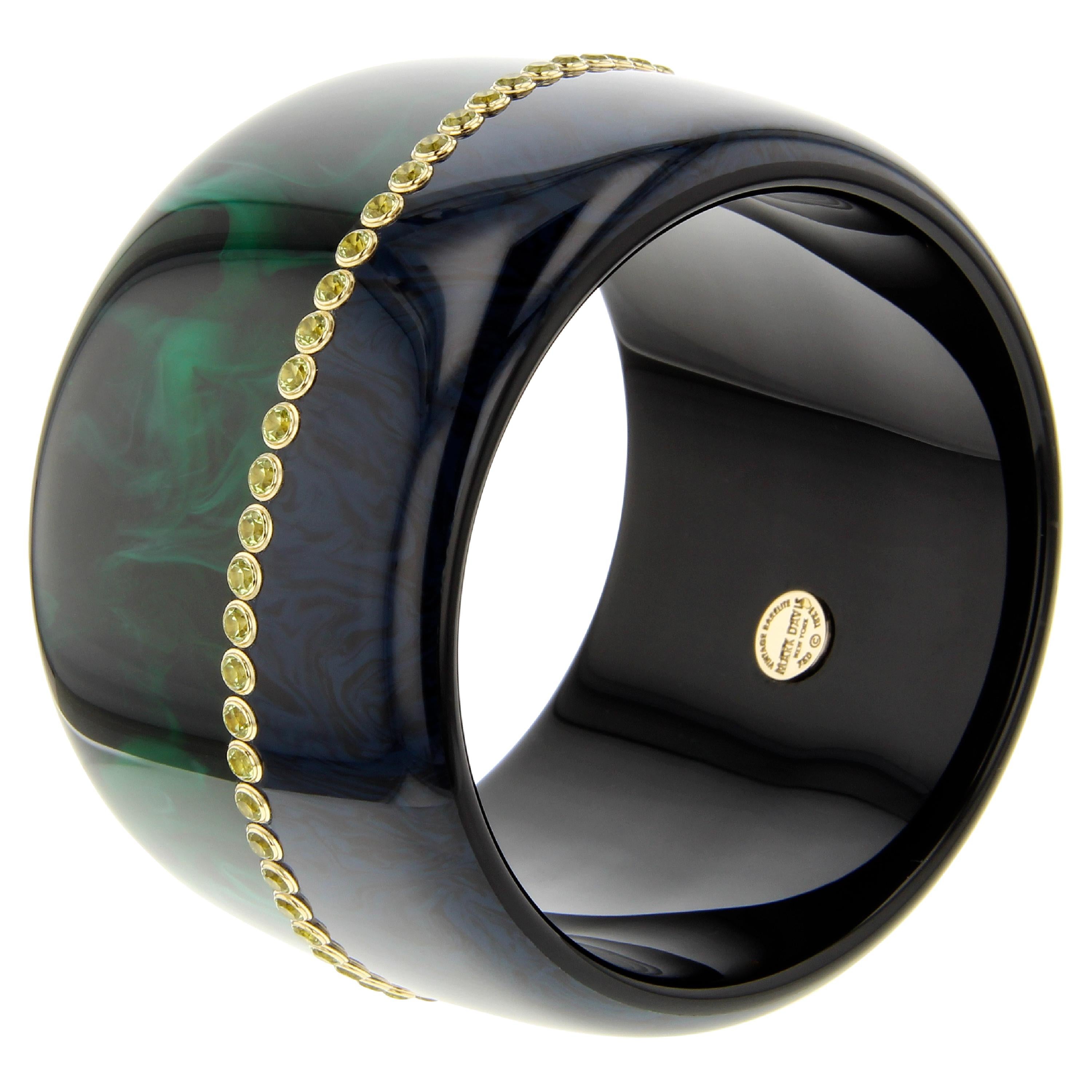 This bold Mark Davis bangle was created by seamlessly joining deep, marbled blue bakelite to an equally rich dark green, marbled bakelite. The asymmetrical border between the two colors has been set with tightly spaced, round peridot set in