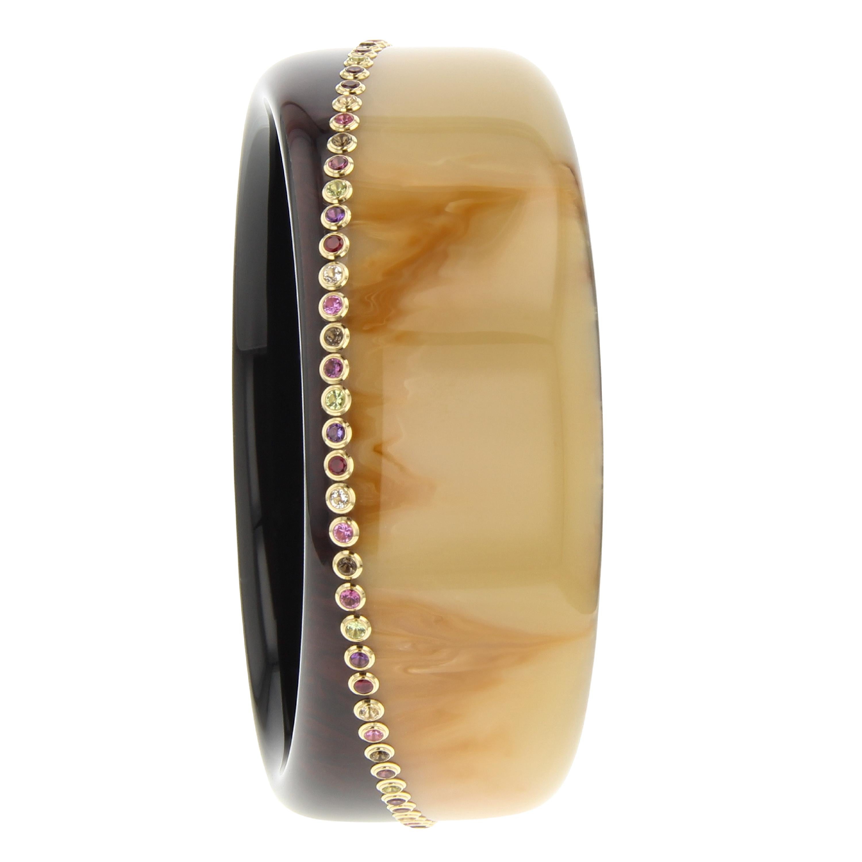 This unique and very graphic Mark Davis bangle was made with two pieces of vintage brown bakelite. The two pieces have been seamlessly joined together creating an asymmetrical line that encircles the bangle. Assorted gemstones in individual 18k gold