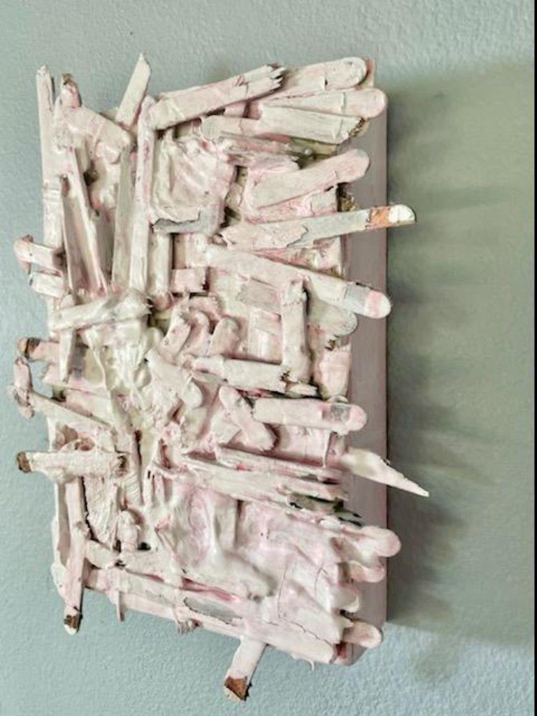 This pale pink and white construction was created with distressed and broken popcycle sticks left out in nature. A combination of plaster and paint secure this abstract sculpture on a box. The texture varies between smooth and rough edge from